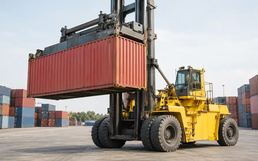 Yellow container top-lift handler with dual front tyres holding a red shipping container.